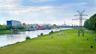 Landschaftsfoto mit Industrieanlage, Fluss und grüner Liegewiese (verweist auf: Umwelt und Gesundheit konsequent zusammendenken)